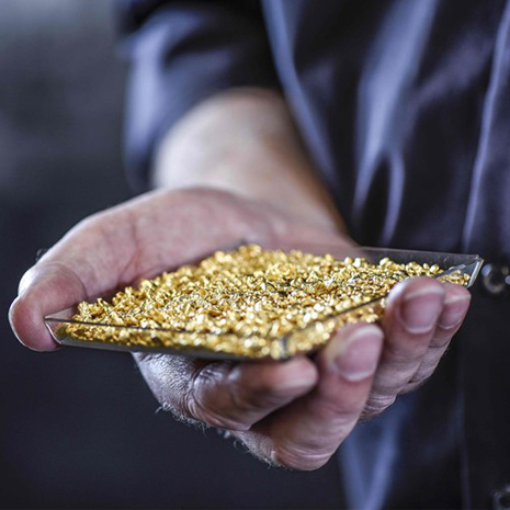 man houdt een bakje met 14 karaat goud korrels vast